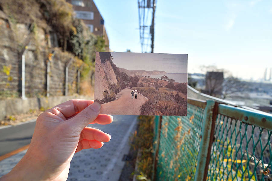 Eine Hand hält ein altes Foto so, dass der echte Hintergrund mit der Landschaft auf dem Foto übereinstimmt.